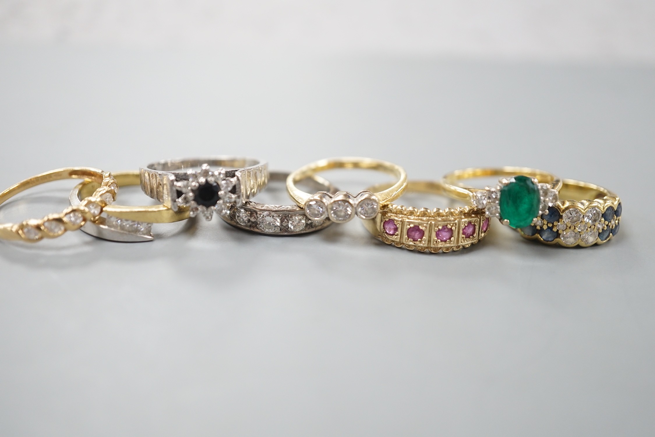 Seven assorted mainly modern 18ct gold or 750 yellow metal and gem set dress rings including emerald and diamond and diamond half eternity, gross weight 26 grams and one 9ct gold and gem set ring, gross 2.9 grams.